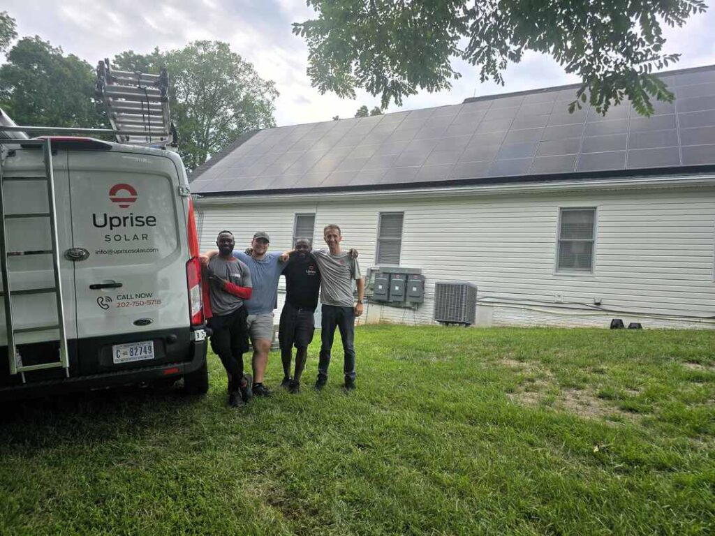 Four members of Uprise Solar's construction team stand next to an Uprise truck in front of a completed solar panel array.